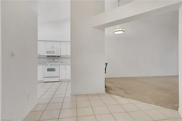 Kitchen featuring white cabinets, high vaulted ceiling, white appliances, light carpet, and light tile patterned floors
