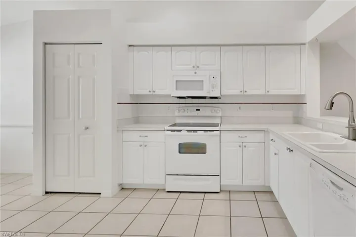 Kitchen featuring white appliances, white cabinetry, light countertops, light tile patterned floors, and backsplash