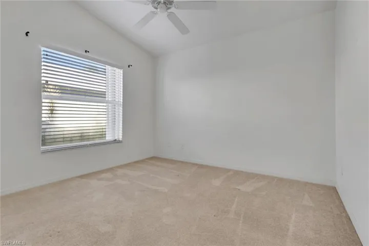 Empty room with light colored carpet, lofted ceiling, and a ceiling fan