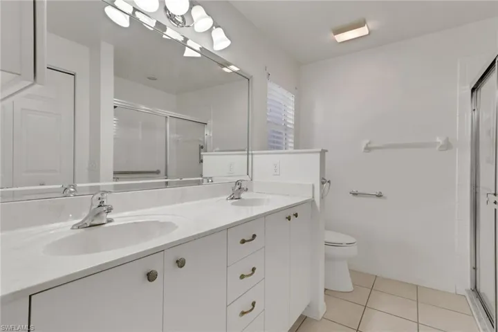 Bathroom with light tile patterned floors, double vanity, and a shower stall