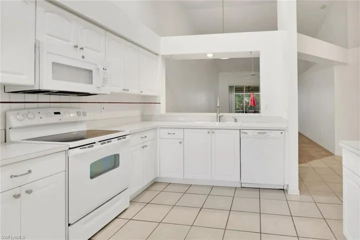 Kitchen featuring white appliances, white cabinets, light countertops, light tile patterned flooring, and backsplash