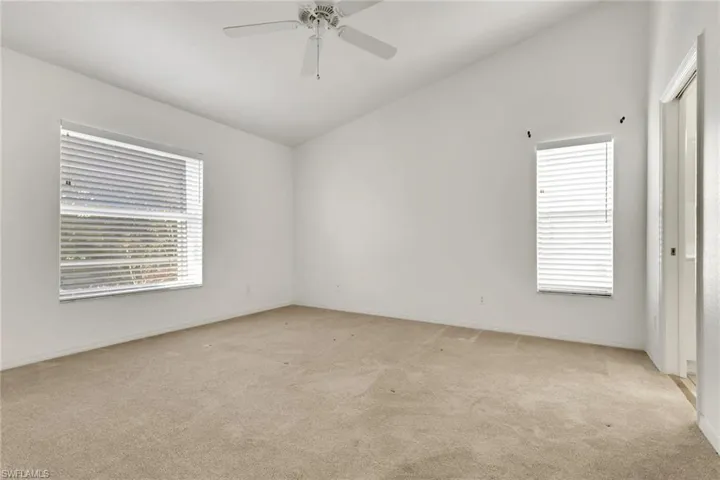 Unfurnished room featuring vaulted ceiling, light carpet, plenty of natural light, and a ceiling fan