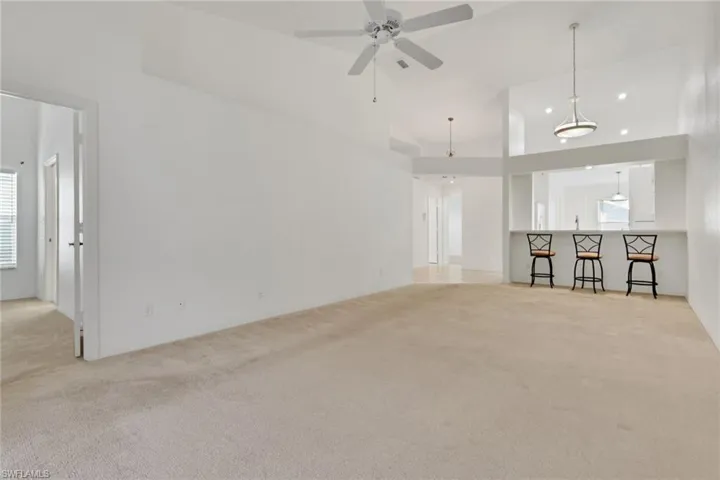 Unfurnished living room featuring light colored carpet, a ceiling fan, and high vaulted ceiling