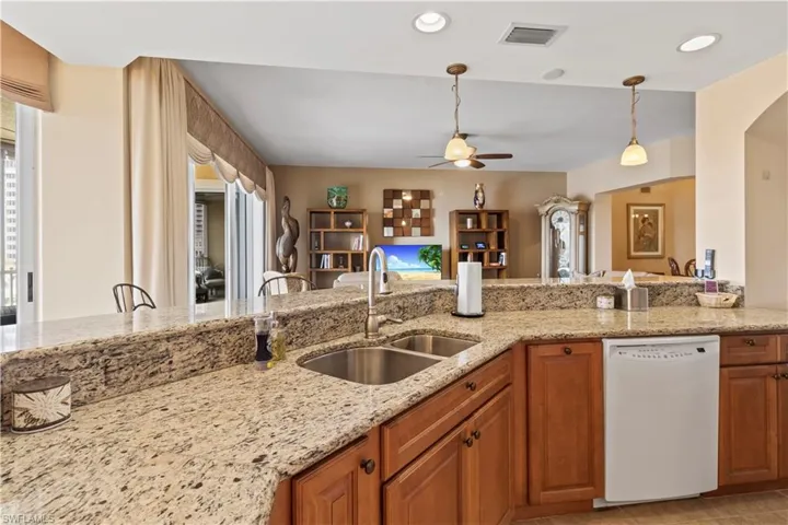 Kitchen with white dishwasher, a ceiling fan, light granite stone countertops, hanging light fixtures, and brown cabinets