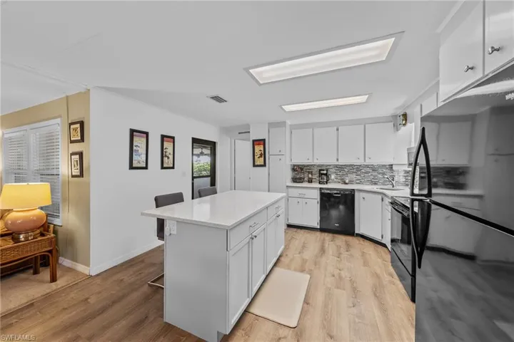 Kitchen featuring light wood-type flooring, white cabinetry, black appliances, a sink, and light countertops