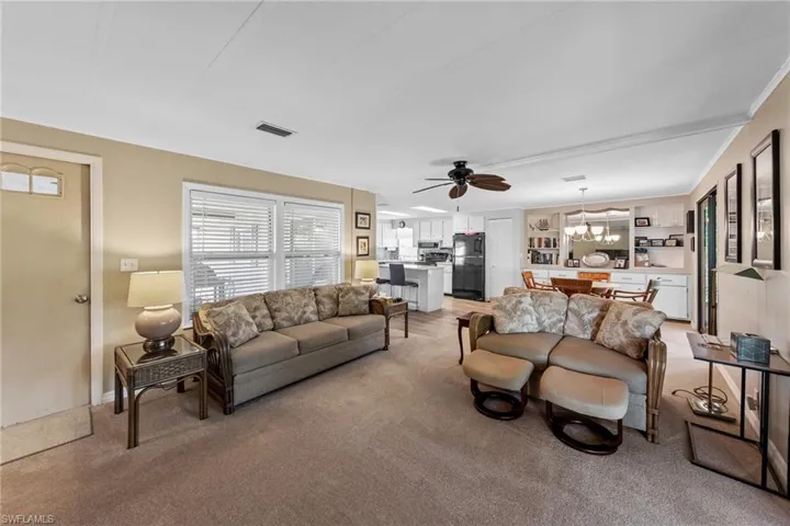 Living room with ceiling fan with notable chandelier, light colored carpet, and visible vents