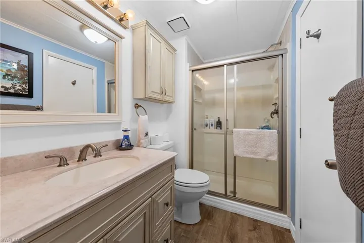 Bathroom with toilet, crown molding, vanity, wood finished floors, and a stall shower