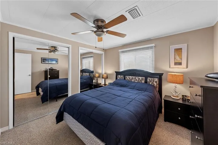 Carpeted bedroom featuring visible vents, a ceiling fan, and crown molding