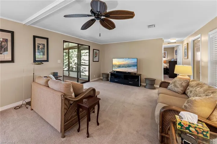 Living room with visible vents, baseboards, ornamental molding, a ceiling fan, and light carpet