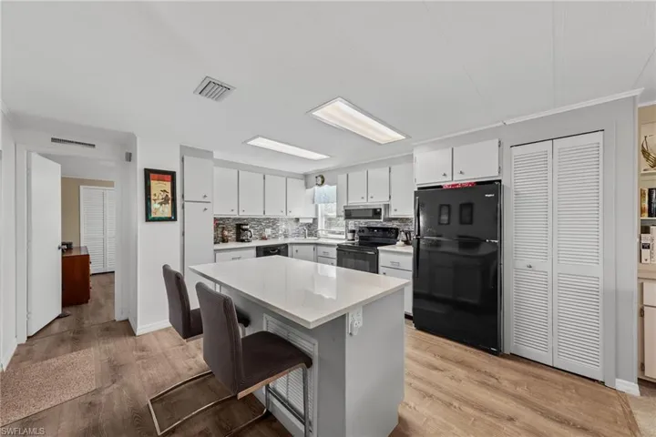 Kitchen with light wood-style flooring, visible vents, black appliances, light countertops, and backsplash