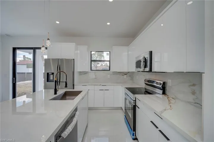 Kitchen featuring modern cabinets, stainless steel appliances, hanging light fixtures, and white cabinetry