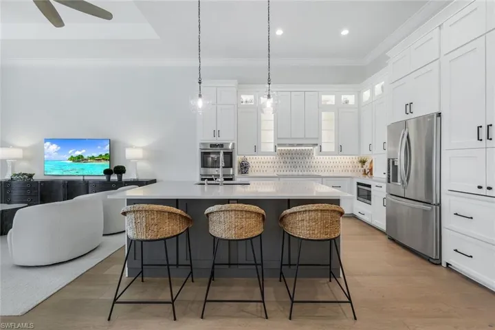 Kitchen featuring a kitchen island with sink, a breakfast bar, appliances with stainless steel finishes, ornamental molding, and tasteful backsplash
