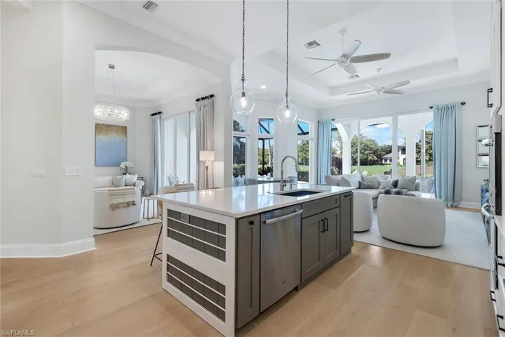 Kitchen featuring open floor plan, a tray ceiling, light wood finished floors, appliances with stainless steel finishes, and light stone counters