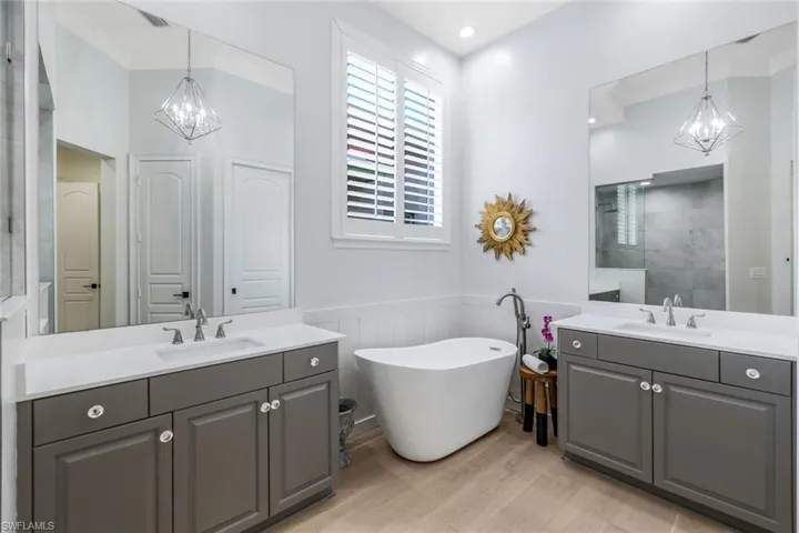 Bathroom featuring a chandelier, two vanities, a soaking tub, a shower stall, and wainscoting