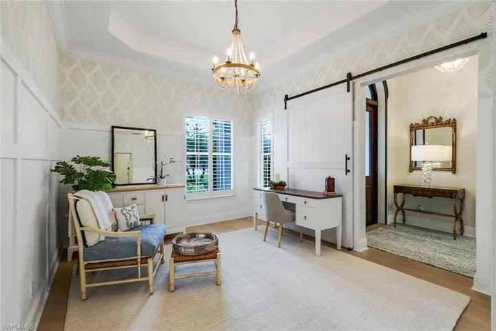 Sitting room featuring a barn door, a chandelier, a desk, wood finished floors, and a tray ceiling