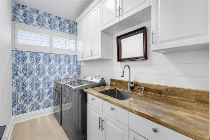 Washroom with wallpapered walls, cabinet space, light wood-style floors, and washer and dryer