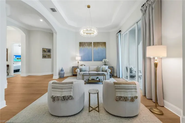 Living area featuring light wood-style flooring, arched walkways, ornamental molding, a chandelier, and a tray ceiling