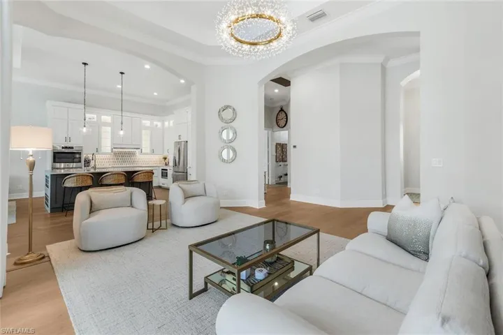 Living area featuring light wood-style floors, crown molding, a chandelier, arched walkways, and recessed lighting