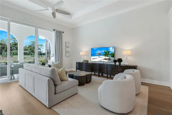 Living area with wood finished floors, ornamental molding, a tray ceiling, and a ceiling fan