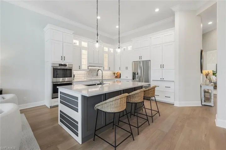 Kitchen with white cabinetry, a breakfast bar area, pendant lighting, glass insert cabinets, and decorative backsplash