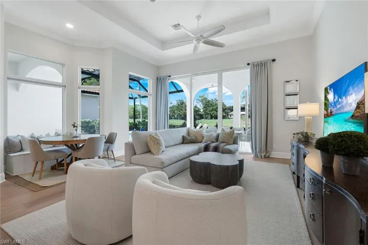 Living area with light wood finished floors, a raised ceiling, and ceiling fan