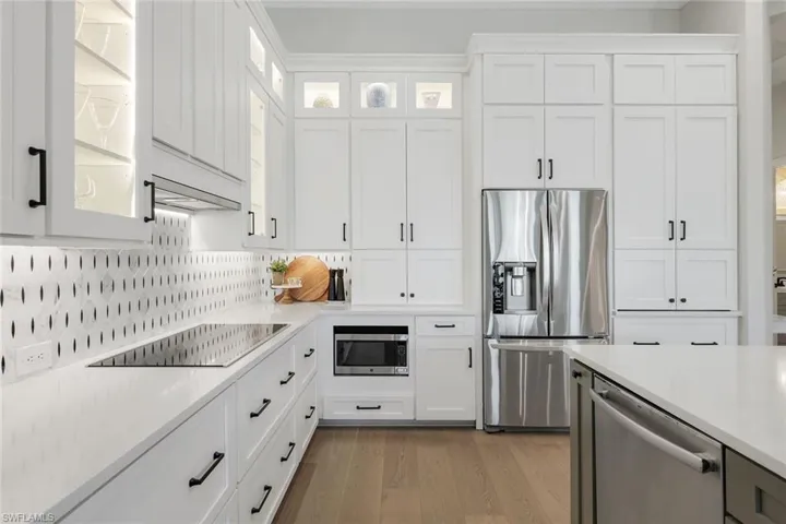 Kitchen with white cabinetry, appliances with stainless steel finishes, light wood-style flooring, glass insert cabinets, and ornamental molding