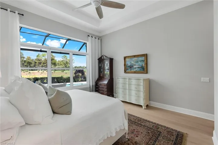 Bedroom with light wood-style flooring, ceiling fan, crown molding, and a tray ceiling