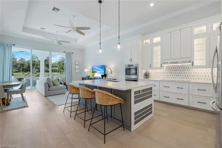 Kitchen featuring white cabinets, decorative light fixtures, a kitchen bar, backsplash, and an island with sink