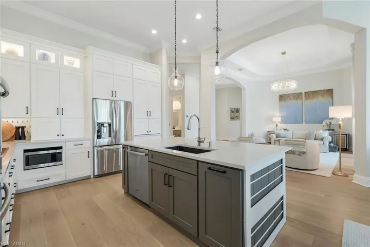 Kitchen with white cabinets, arched walkways, light wood-style flooring, appliances with stainless steel finishes, and a chandelier