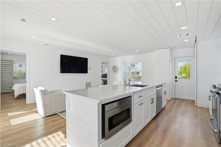 Kitchen featuring white cabinets, a kitchen with sink, wood ceiling, light wood-style floors, and light stone counters Virtually edited