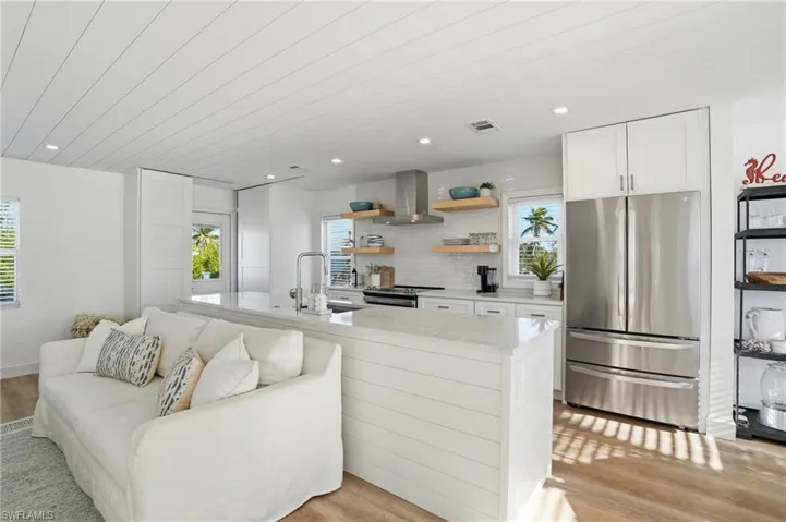 Kitchen featuring stainless steel appliances, light stone countertops, light wood-style flooring, white cabinetry, and extractor fan Virtually Edited