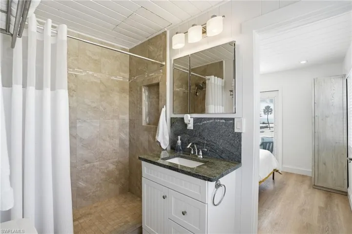 Ensuite bathroom featuring vanity, a shower stall, light wood-style floors, and tasteful backsplash Virtually Edited