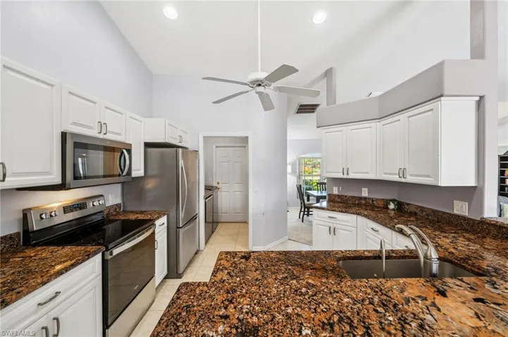 Kitchen with stainless steel appliances, white cabinetry, dark stone countertops, high vaulted ceiling, and a ceiling fan