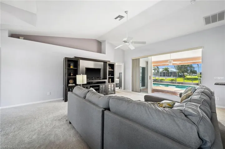 Carpeted living room featuring ceiling fan, high vaulted ceiling, and a sunroom