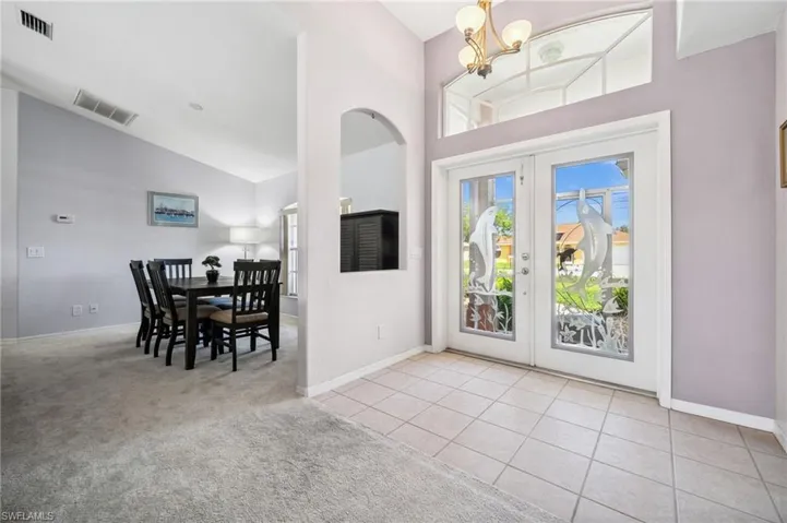 Foyer with french doors, light carpet, high vaulted ceiling, light tile patterned floors, and a chandelier