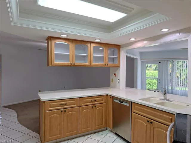 Kitchen featuring light wood cabinetry with glass-front upper cabinets, white countertops, and white tile flooring