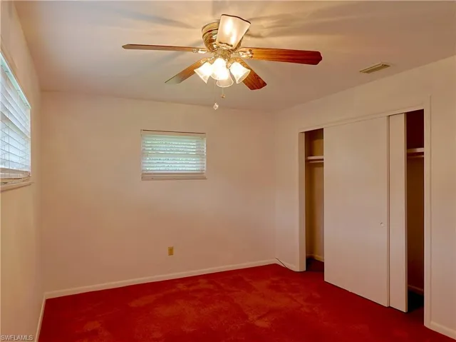 Interior room featuring red carpeting, white painted walls, and a ceiling fan with integrated lighting
