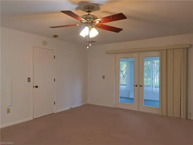 Interior room featuring neutral wall paint, light brown carpeting, a ceiling fan with light fixture, and double glass-paneled French doors