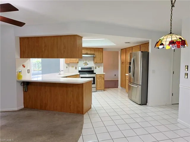 Open-concept kitchen featuring light-toned wood cabinetry, stainless steel appliances, a breakfast bar, white tile flooring, and a skylight