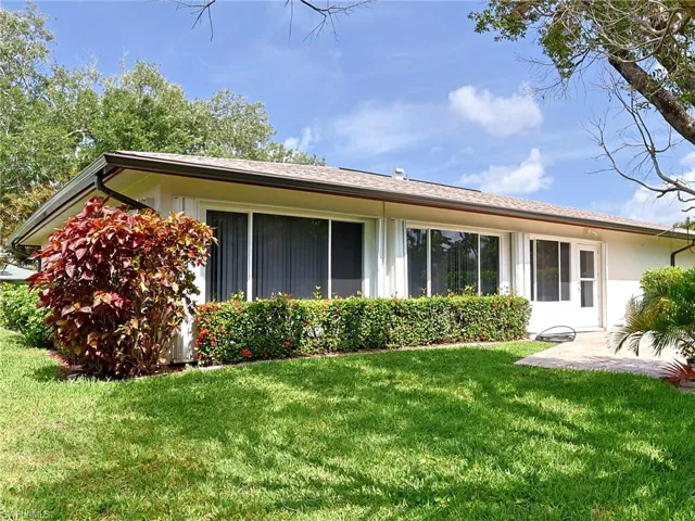 Exterior featuring white stucco siding, a brown shingle roof, and dark brown gutters