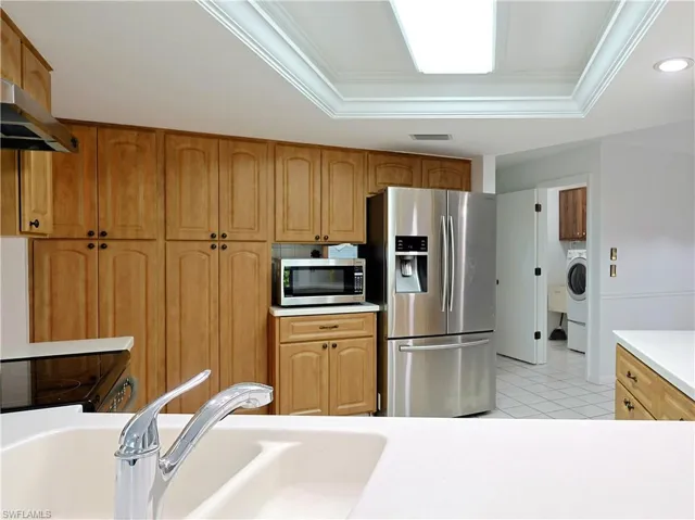 Kitchen featuring extensive wood cabinetry, white countertops, stainless steel appliances, and a recessed tray ceiling with flush lighting