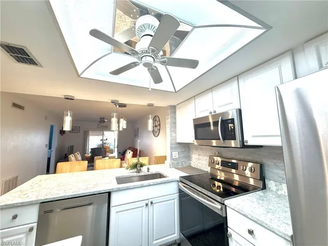 Kitchen with stainless steel appliances, a peninsula, white cabinetry, decorative backsplash, and decorative light fixtures