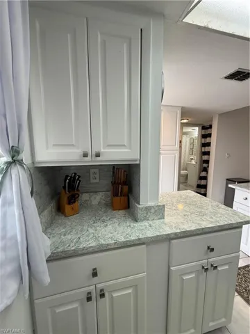 Kitchen featuring white cabinetry, light stone countertops, and backsplash