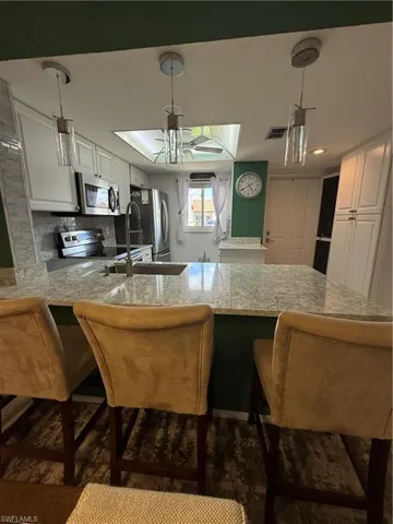 Kitchen with a breakfast bar area, a peninsula, white cabinetry, and hanging light fixtures