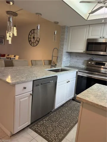 Kitchen featuring white cabinets, stainless steel stove, pendant lighting, and light stone counters