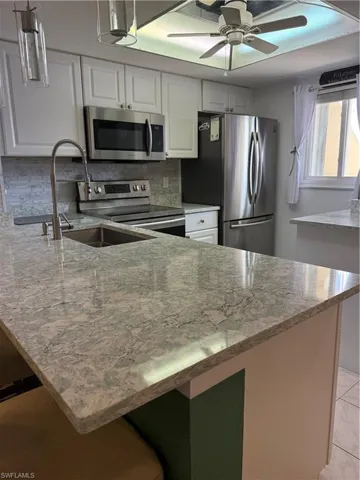 Kitchen with white cabinets, stainless steel appliances, light stone countertops, and backsplash