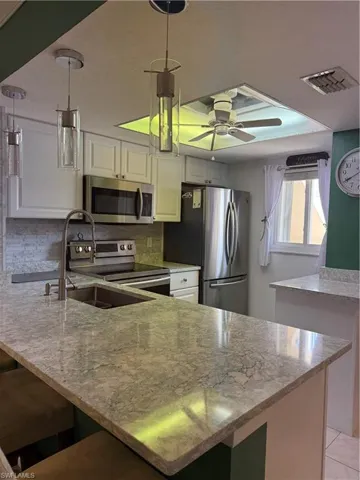 Kitchen featuring light stone counters, stainless steel appliances, white cabinets, a peninsula, and a ceiling fan