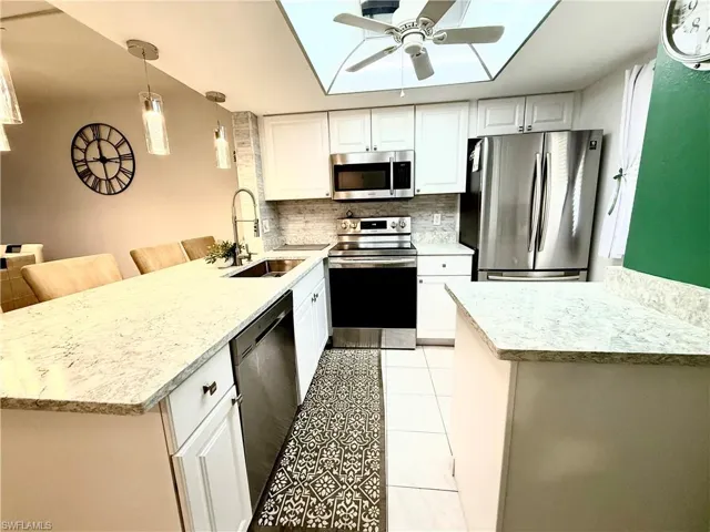 Kitchen featuring a peninsula, stainless steel appliances, decorative light fixtures, and white cabinetry