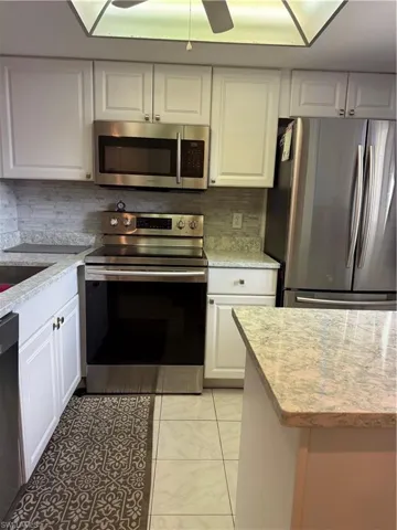 Kitchen featuring stainless steel appliances, white cabinets, light stone countertops, a ceiling fan, and decorative backsplash