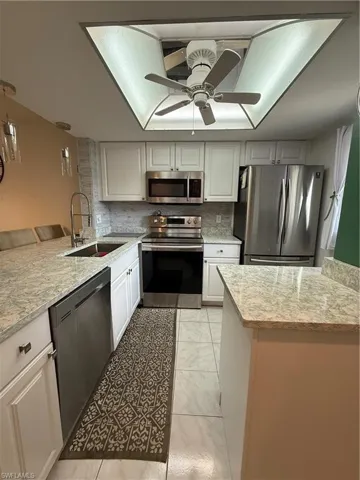 Kitchen featuring stainless steel appliances, white cabinetry, decorative backsplash, and hanging light fixtures
